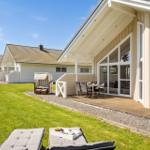Terrasse mit Tisch und Stühlen, Gartenliegen und Strandkorb vor einem Ferienhaus.