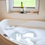 Badewanne mit Schaum, Wein und Glas vor Fenster