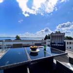 Terrace with table, chairs, and lounge under blue sky with water view.