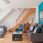 Living room with sofa, armchair, and wooden staircase. Blue wall and wooden floor.