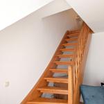 Wooden stairs with handrail lead to upper level. Wall color white and turquoise.
