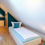 Bedroom with sloped ceiling, bed with pillows, and wooden floor.
