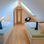 Two beds with pillows, wooden floor, skylight, and chair in attic room.