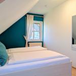 Bedroom with sloped ceiling, bed, window, and mirror on the wall.