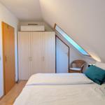 Bedroom with sloped ceiling, bed, wardrobe, and seating area.
