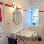 Bathroom with sink, toilet, and shower. White tiles with red stripe.