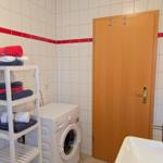 Washing machine, towel rack, and sink in bathroom with white tiles and red stripe.