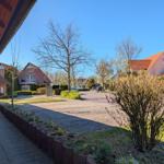 View of a paved courtyard with houses and trees under a blue sky.