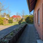 Paved path beside red brick house with flower bed and green areas