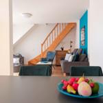 Dining area with fruit bowl, view into living room with wooden staircase and sofa.