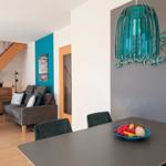 Dining area with table and chairs, wall decor, and view into living room with sofa and staircase.