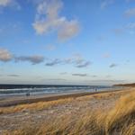 Beach with dunes and sea under blue sky with white clouds.