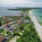 View of coastal town with beach, marina, and green backyards.
