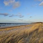 Beach with dunes, sea, and sky with clouds. People walk along the shore.
