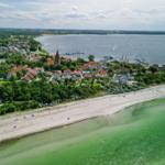 Aerial view of beach, coastal town, and harbor with boats.