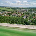 Aerial view of a coastal town with beach, green water, and surrounding fields.