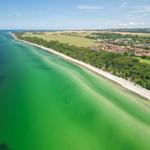 Aerial view of a coastline with beach, green water, and a village with red roofs.