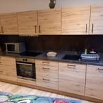 Küche mit Holzschränken, Spüle und Herd. Auf Arbeitsplatte stehen Geschirr und Küchenutensilien.
