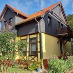 Haus mit gelbem Sockel und dunklem Dach, umgeben von Grün und Blumen.