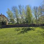 Lawn area with blooming trees and stone wall. A house with red roof is visible in the background.