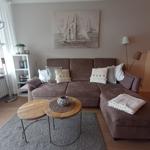 A living room with a brown sofa, two round wooden tables, and wall art.