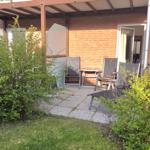 Terrasse mit Sitzgelegenheiten und Garten. Hintergrund: Backsteinmauer und offene Tür.