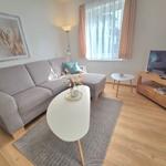 Ein Wohnzimmer mit grauem Sofa, weißem Tisch und Holzboden.