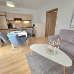 Wohnzimmer mit Sofa, Esstisch und Küchenbereich. Holzboden und helle Wände.