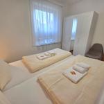 Zimmer mit Doppelbett, Schrank und Stuhl. Fenster mit weißen Vorhängen.