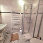 Badezimmer mit Dusche, Waschbecken und Toilette. Fliesenwand mit dunkler Zierleiste.