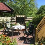 Terrasse mit Tisch, Stühlen und Liegestuhl unter Bäumen.