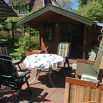 Terrasse mit Tisch, Stühlen und Hütte im Hintergrund.