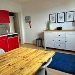 Küche mit roten Schränken und Holztisch. Weiße Kommode mit Bildern und Lampe.