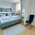 Schlafzimmer mit Bett, Stuhl und Fenster. Wandbild zeigt Strand.