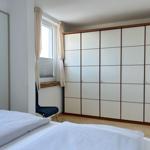 Schlafzimmer mit Bett, Kleiderschrank und Fenster mit Vorhängen.