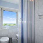 Badezimmer mit Dusche, Toilette und Fenster mit Blick auf Landschaft.