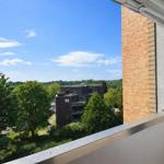 Balkon mit Blick auf grüne Bäume und ein modernes Gebäude unter blauem Himmel.