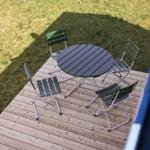 Rundtisch mit vier grünen Stühlen auf Holzterrasse mit Grasfläche.