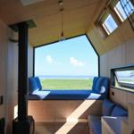 Wohnraum mit Sitzbank, Kamin und Aussicht auf Grasfläche und Meer.