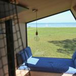 Ein Fensterblick auf den Strand und das Meer. Blaue Matratze und Kissen.