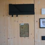 Holzwand mit Tür, QR-Code für Gästeprogramm und Bedienelemente.