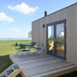 Terrasse mit Tisch und Stühlen vor einem Holzhaus mit Meerblick.