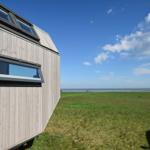 Holzhaus mit Fenstern am Strand unter blauem Himmel mit Wolken.