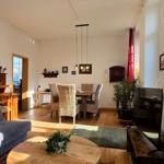 Living and dining area with sofa, dining table, and TV. Wooden floor and plants.