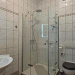 Bathroom with shower, sink, and toilet. Tiled walls and plants visible.