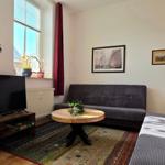 Living room with sofa, TV, and table. Window with curtains. Wall pictures and lamp.