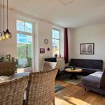 Living room with dining table, sofa, and windows. Wooden floor and plants.