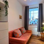 A room with an orange sofa, wooden floor, and window with curtains.