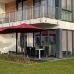 Terrasse mit Tisch, Stühlen und roten Sonnenschirmen vor modernem Haus mit Balkon.