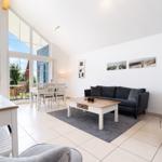 Living room with sofa, coffee table, and TV. Large windows with sea view.